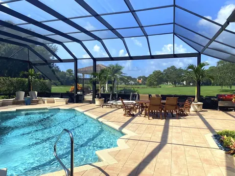 Black mansard pool cage over a pool and patio dining set, golf course fairway and palms beyond the screen